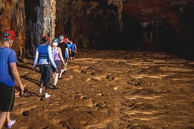A line of visitors in helmets walking across the patterned floor of a dry cave chamber