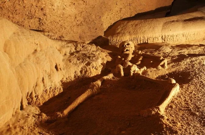 A calcite-coated skeleton lying on the floor of a golden-lit cave chamber