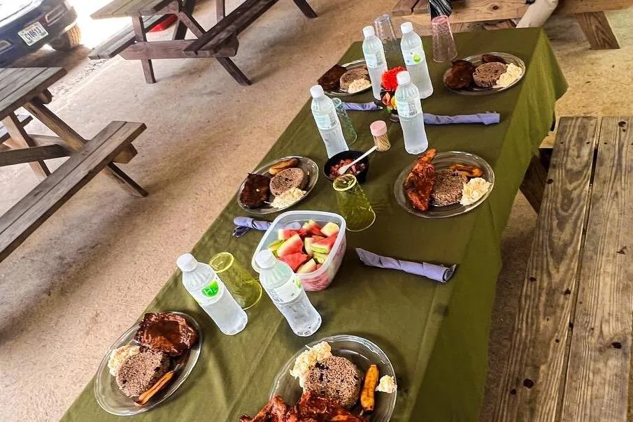A picnic table laid with plates of Belizean food, fruit and bottled water