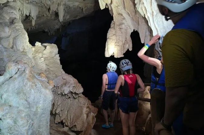 Visitors in helmets and life vests, seen from behind, walking into a cave with pale formations