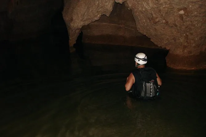 A caver in a white helmet wading chest-deep through dark cave water